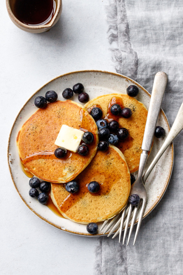 Overhead, plate of Blueberry Sourdough Pancakes with pat of butter, fresh blueberries and pot of maple syrup