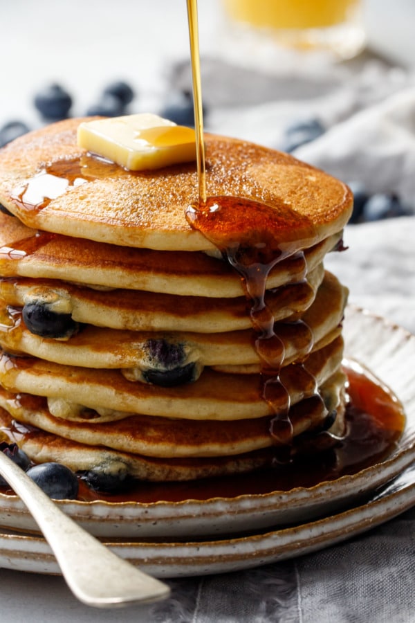 Closeup drizzle of maple syrup on a tall stack of Blueberry Sourdough Pancakes