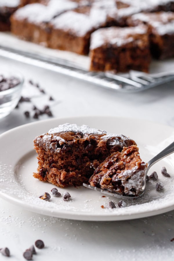 One square of oatmeal chocolate chip cake with a forkful taken out to show the moist texture