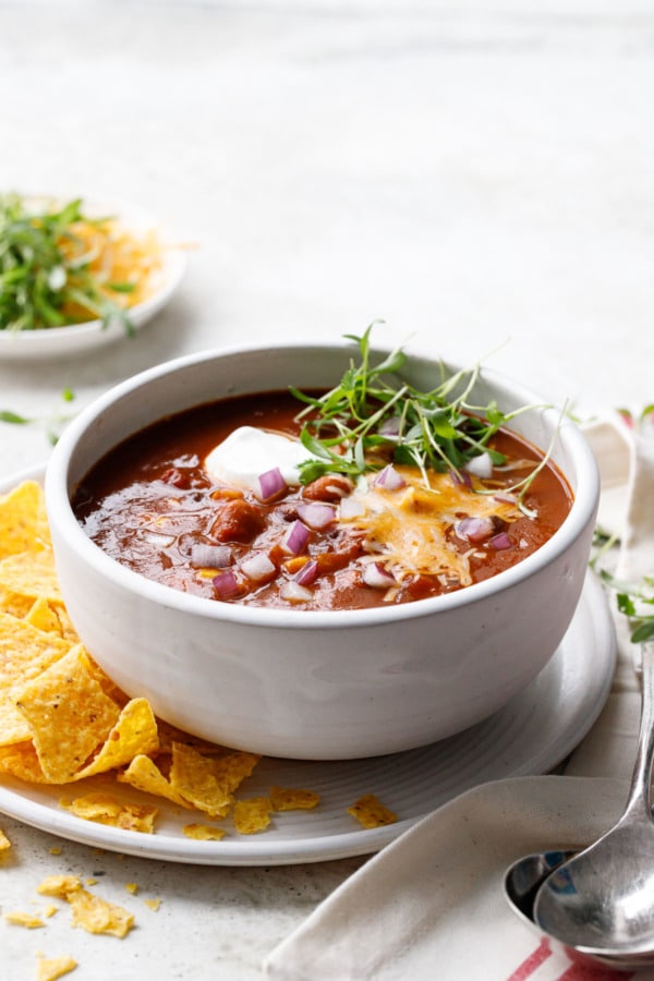 Single bowl of Vegetarian Pumpkin & Three-Bean Chili, with tortilla chips and a bowl of toppings