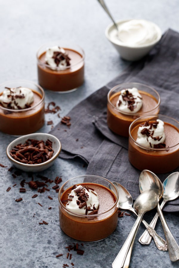 Glass ramekins filled with Chocolate Pumpkin Pot de Creme on a dark gray background