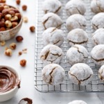 Stuffed Hazelnut Amaretti Cookies on a wire rack, bowl of hazelnuts and nutella on the side