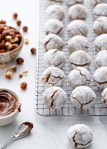 Stuffed Hazelnut Amaretti Cookies on a wire rack, bowl of hazelnuts and nutella on the side