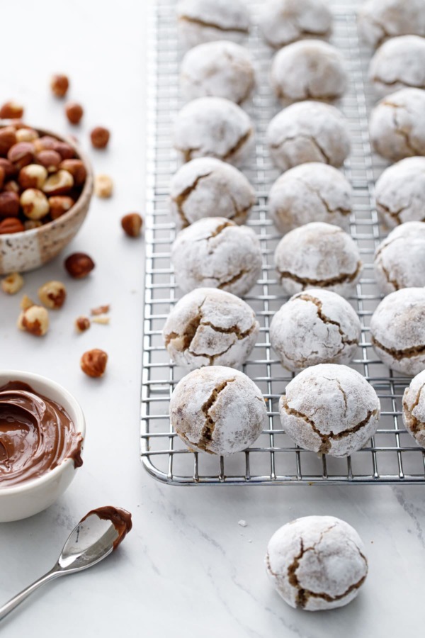 Stuffed Hazelnut Amaretti Cookies on a wire rack, bowl of hazelnuts and nutella on the side