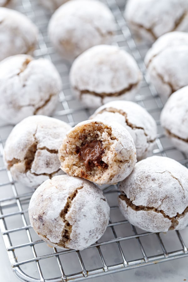 Stuffed Hazelnut Amaretti Cookies on a wire rack, one cookie with a bite out of it showing the Nutella filling inside