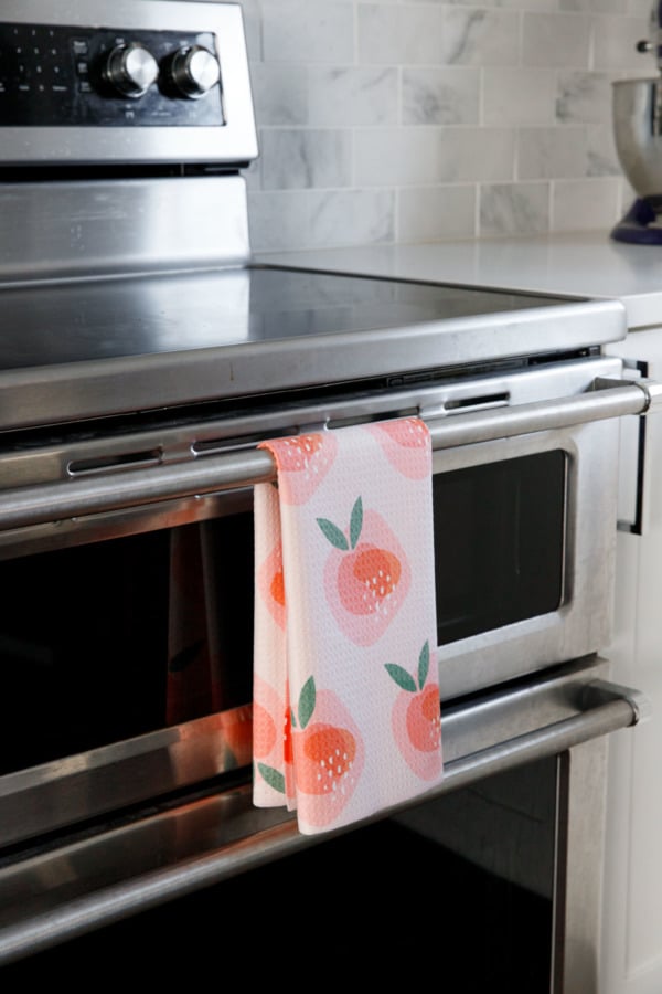 Peachy pattern dish towel hanging on an oven door