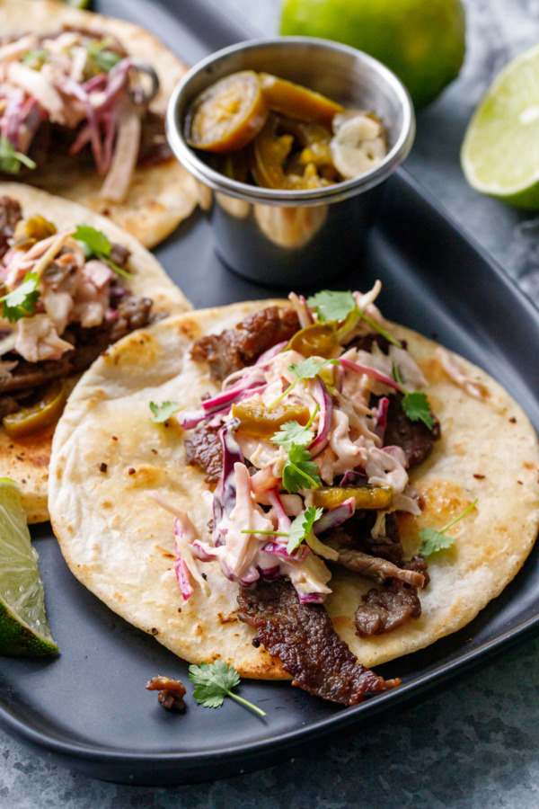 Closeup of the filling of a steak street taco, topped with micro cilantro leaves and pickled jalapenos