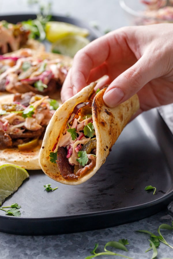 Hand lifting a steak street taco off of a black platter