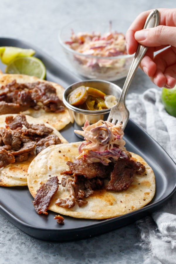 Fork topping a steak street taco with tangy chipotle coleslaw