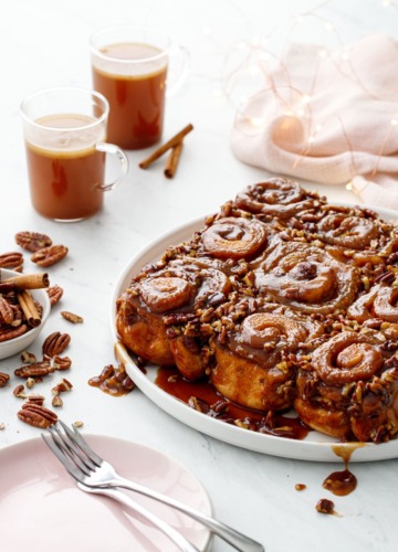 Platter of gooey sticky buns with pecans, cups of hot buttered rum in the background