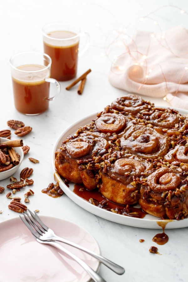 Platter of gooey sticky buns with pecans, cups of hot buttered rum in the background