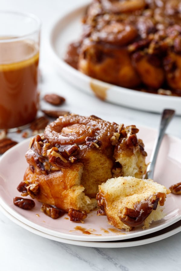 Forkful of hot buttered rum sticky bun on a pink plate, showing the light and fluffy texture of the dough