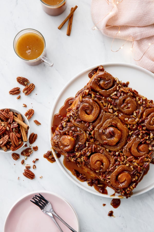 Overhead Platter of gooey sticky buns with pecans, cups of hot buttered rum, and christmas twinkle lights