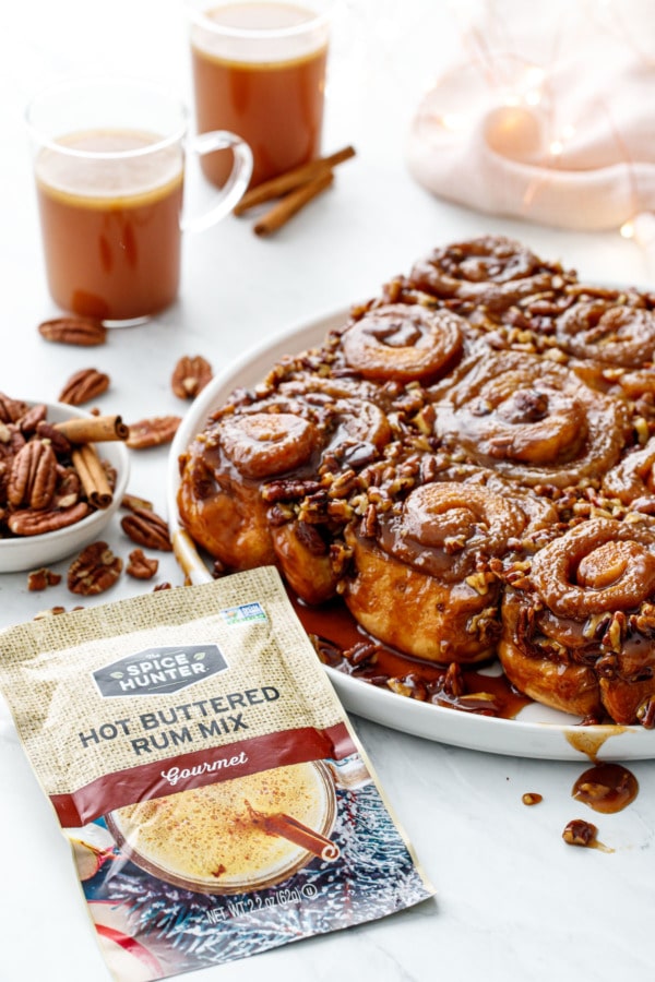 Platter of gooey sticky buns with pecans, cups of hot buttered rum, showing the Hot Buttered Rum packet from The Spice Hunter