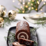 Sliced Chocolate Chestnut Christmas Cake Roll, dusted with sugar, christmas lights and ornaments blurred in the background