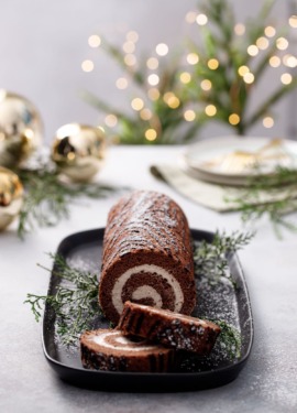 Sliced Chocolate Chestnut Christmas Cake Roll, dusted with sugar, christmas lights and ornaments blurred in the background