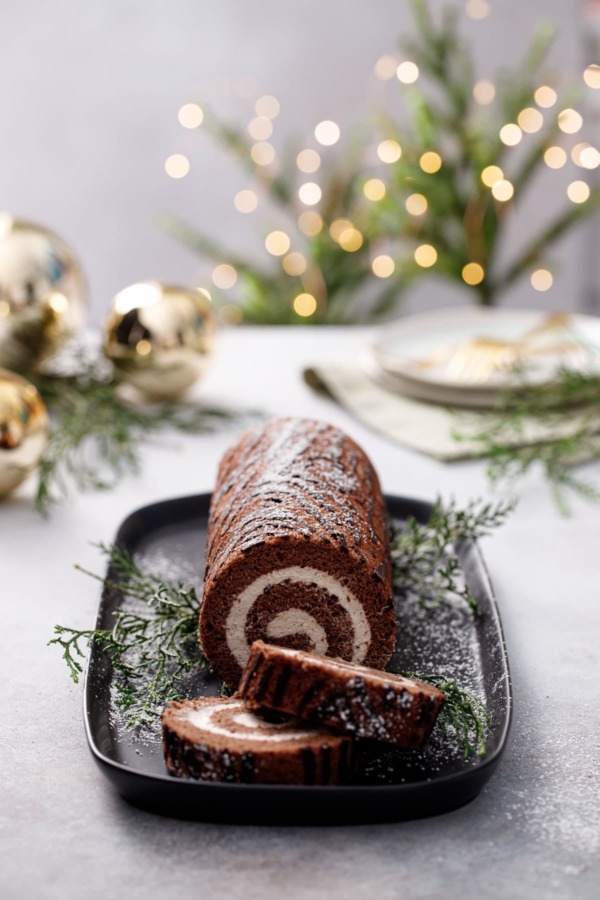 Sliced Chocolate Chestnut Christmas Cake Roll, dusted with sugar, Christmas lights and ornaments blurred in the background