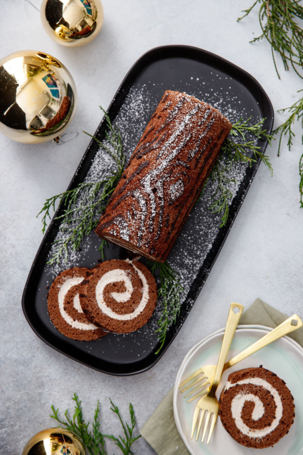 Overhead: wood grain yule log cake roll, with greenery and gold Christmas ornaments