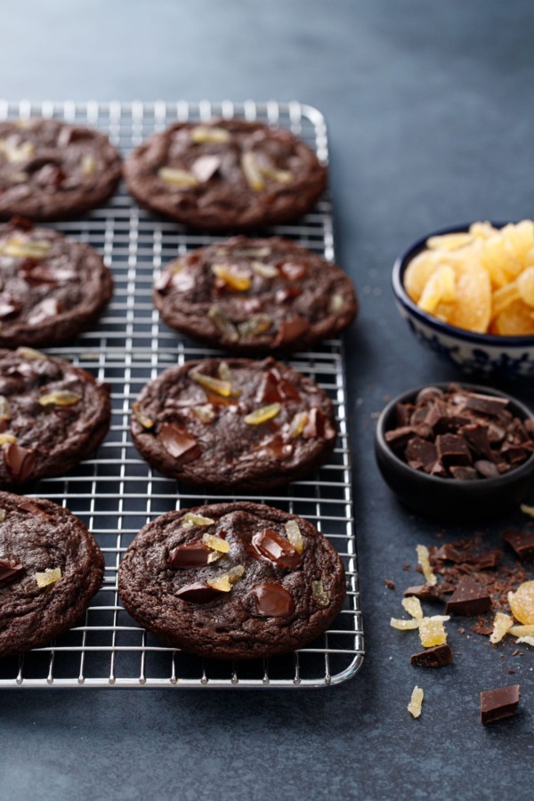 Rows of Double Dark Chocolate Ginger Cookies on a wire rack, with bowls of chopped chocolate and candied ginger.