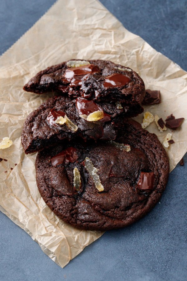 Double Dark Chocolate Ginger Cookies on natural parchment, one cookie broken in half to show gooey interior texture.