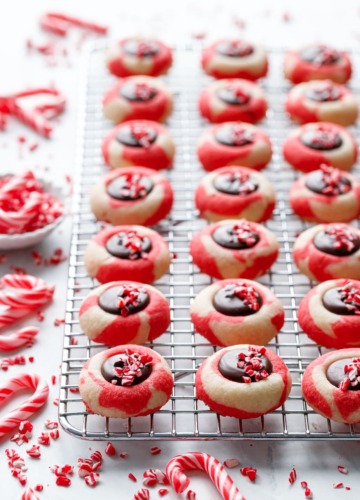 Rows of Chocolate Peppermint Thumbprints on a wire rack, crushed candy canes scattered around