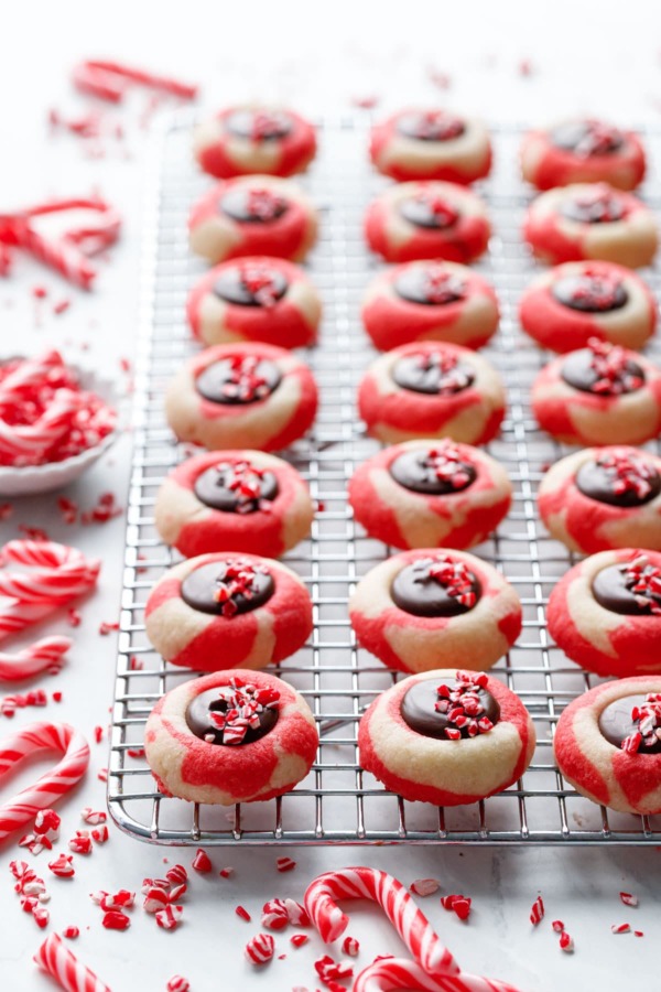 Rows of Chocolate Peppermint Thumbprints on a wire rack, crushed candy canes scattered around