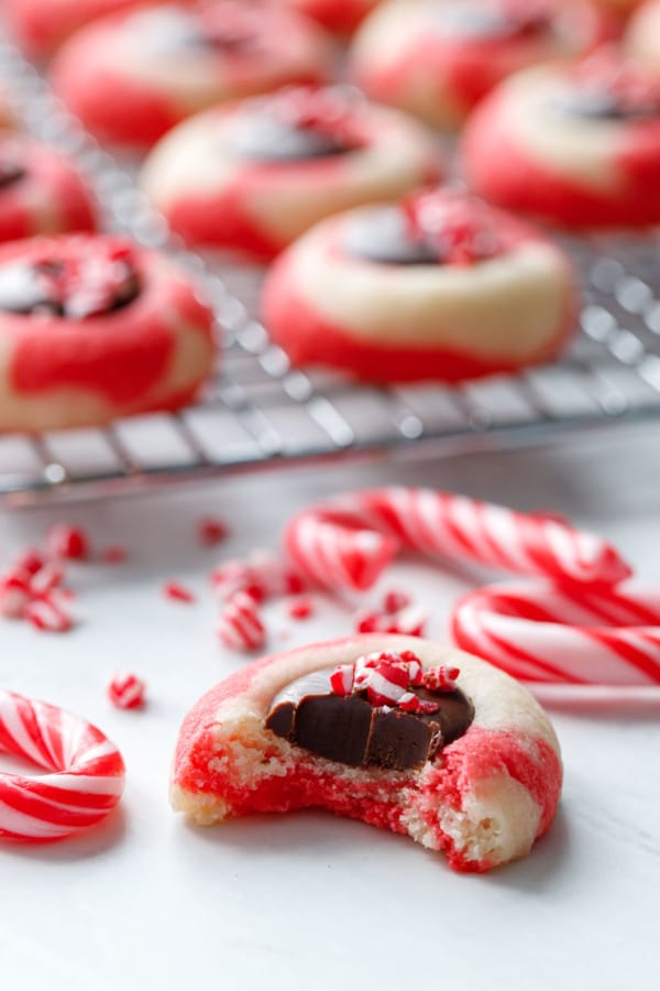 Closeup bite out of a Chocolate Peppermint Thumbprint cookie, with candy canes and out of focus cookies in the background