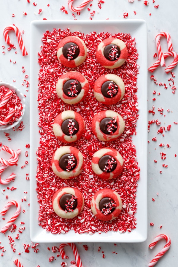 Overhead, two rows of red and white swirl thumbprint cookies on a bed of crushed candy canes