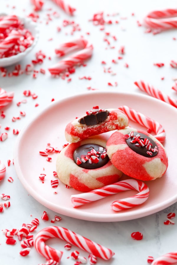 Pink plate with three Chocolate Peppermint Thumbprints, mini candy canes and crushed ones scattered around