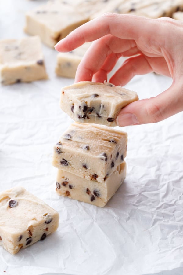 Hand lifting a square of Chocolate Chip Cookie Dough Fudge from a stack