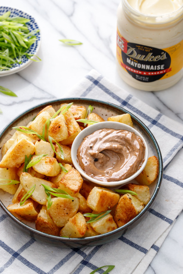 Bowl of golden brown crispy potatoes, with a dish of black garlic aioli, jar of Duke's Mayonnaise, and sliced green onions