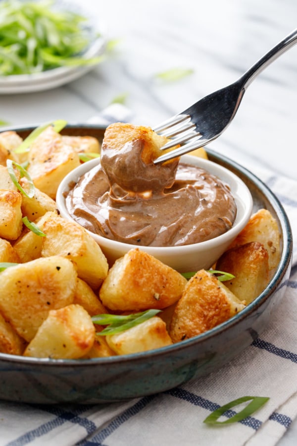 Fork dipping a crispy piece of potato into a dish of black garlic aioli