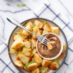 Overhead dish of crispy potatoes with black garlic aioli, sliced green onions on the side