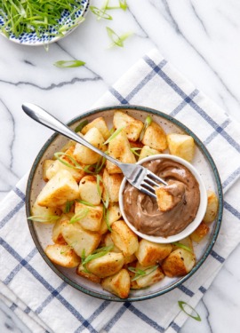 Overhead dish of crispy potatoes with black garlic aioli, sliced green onions on the side