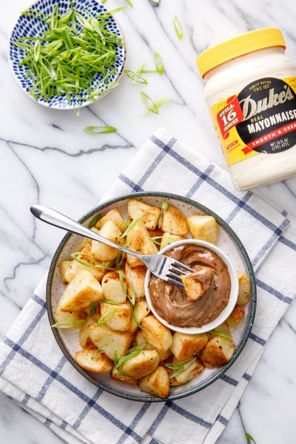 Overhead dish of crispy potatoes with black garlic aioli made with Duke's Mayonnaise, sliced green onions on the side