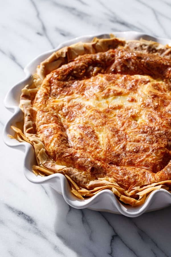 Deep dish quiche in a white ruffled pie dish, on a marble background in direct sunlight