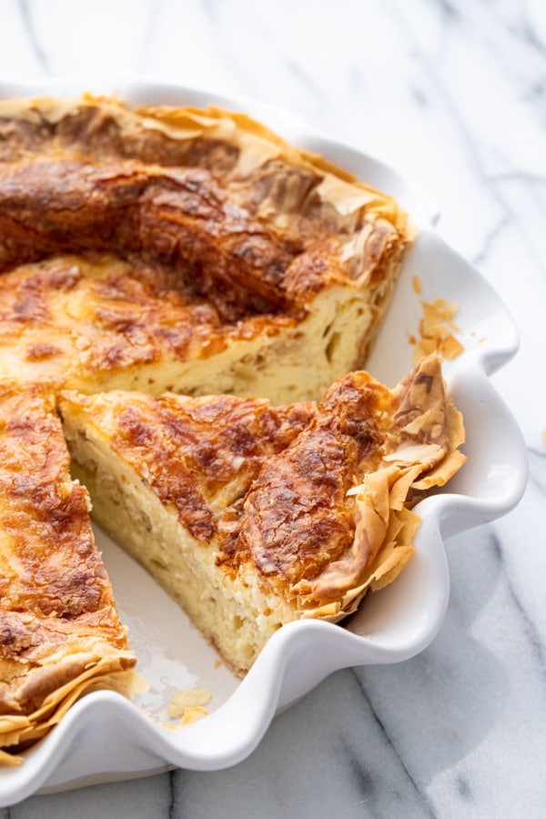 White deep dish pan with sliced Cheese & Caramelized Onion Quiche