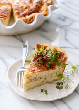Slice of Cheese & Caramelized Onion Quiche topped with microgreens on a white ceramic plate