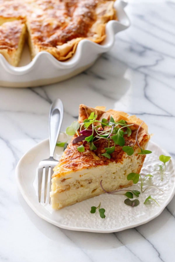 Slice of Cheese & Caramelized Onion Quiche topped with microgreens on a white ceramic plate