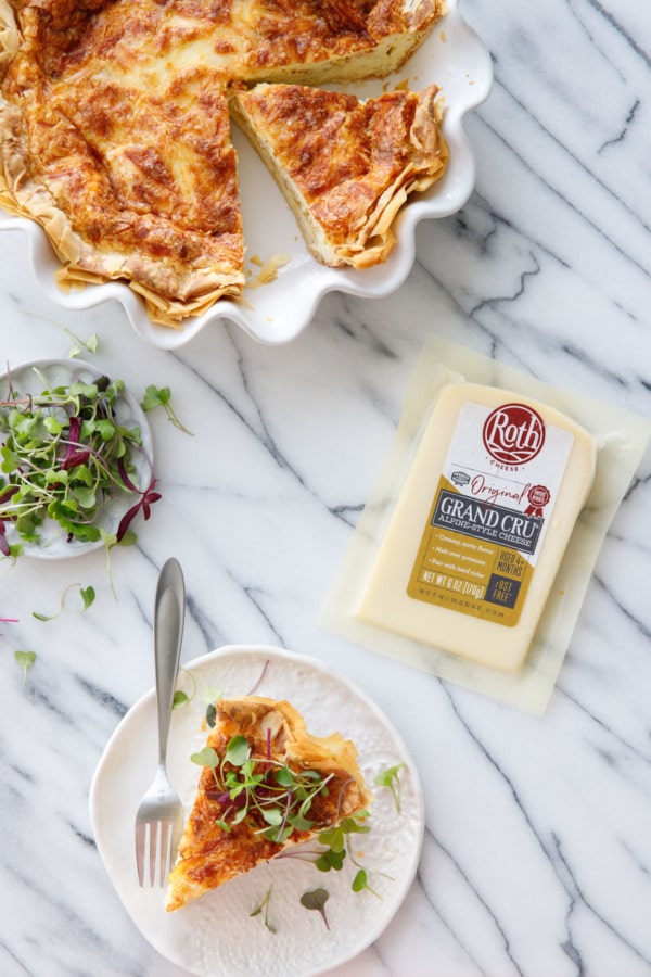 Overhead on marble, Quiche in white ruffled pie pan, plate with slice, and block of Roth Grand Cru cheese