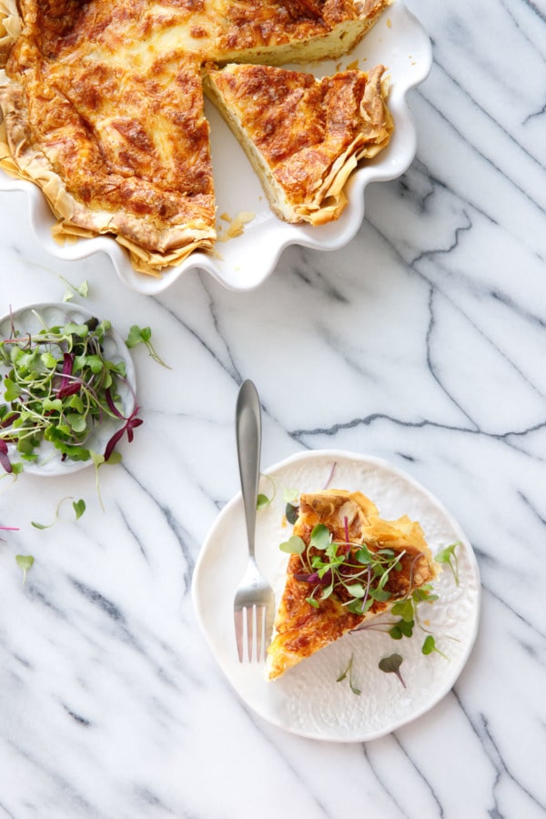 Overhead on marble, Quiche in white ruffled pie pan, plate with slice, and dish of microgreens