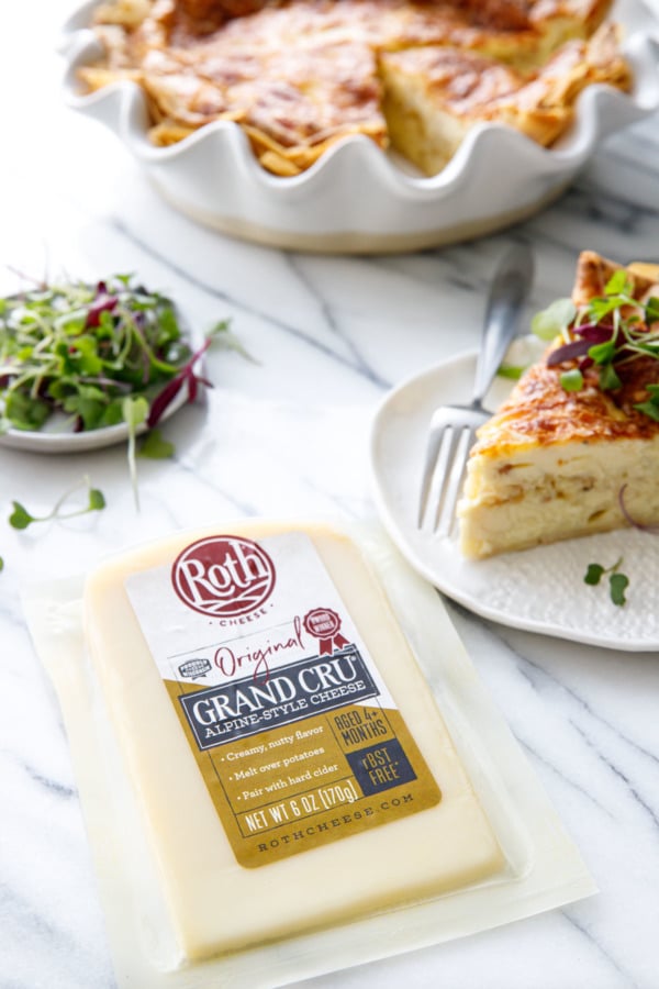 Block of Roth Grand Cru cheese with a plate with slice of quiche and microgreens