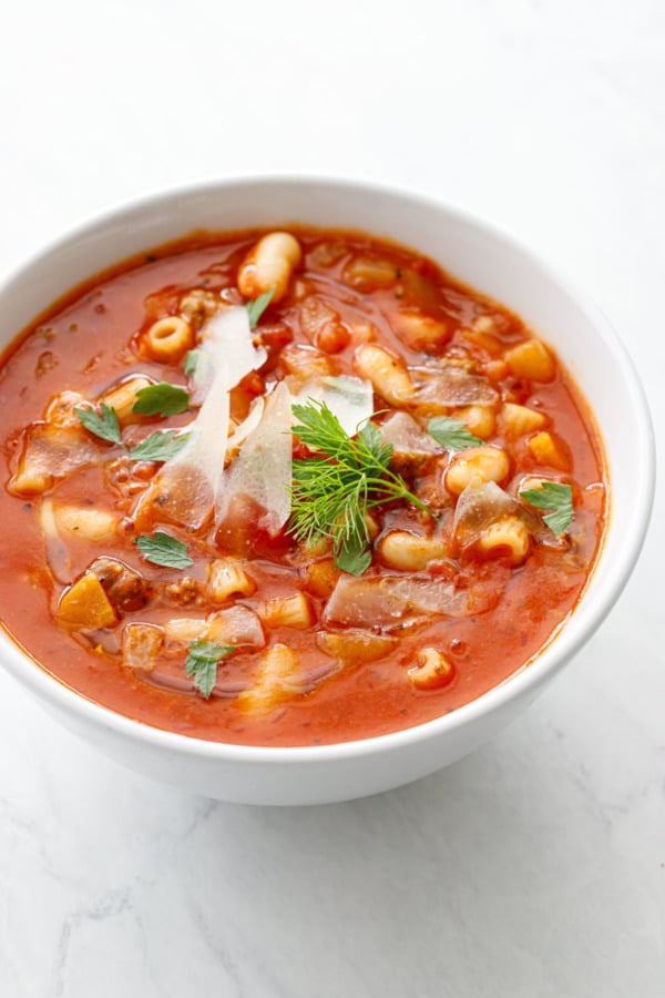 White bowl with Pasta e Fagioli, topped with parmesan shavings and fresh parsley