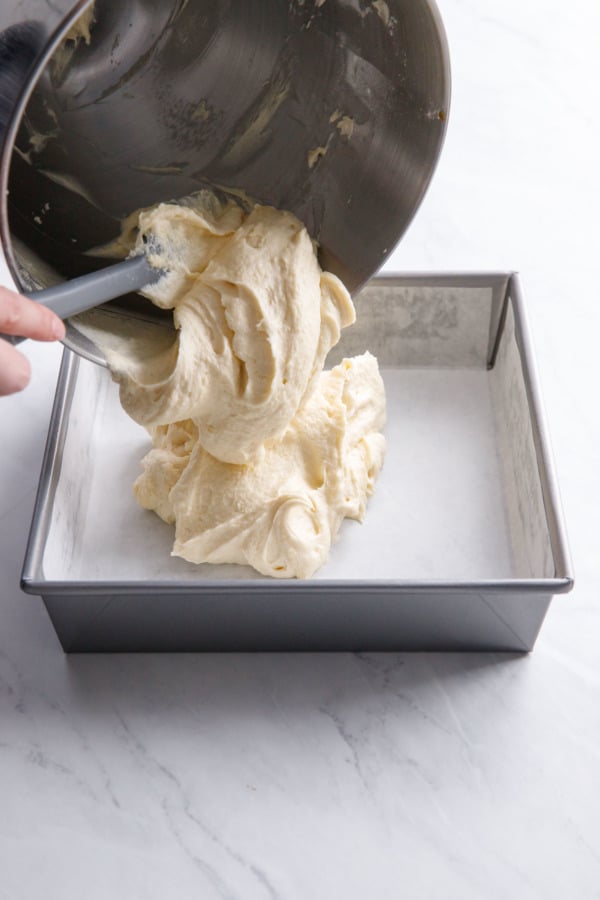 Pouring yellow cake batter into square baking pan