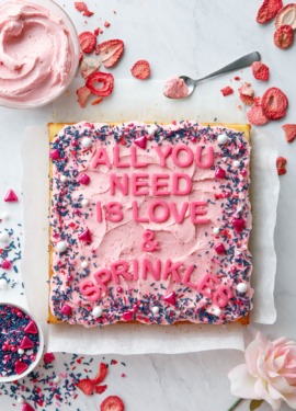 Overhead, Square cake with pink frosting and sprinkles, letters that read All You Need is Love & Sprinkles