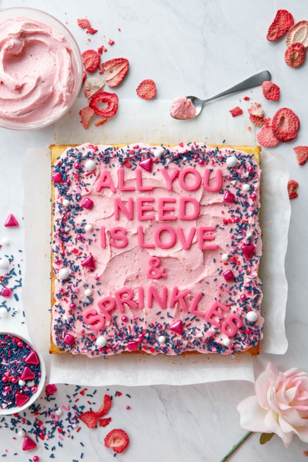 Overhead, Square cake with pink frosting and sprinkles, letters that read All You Need is Love & Sprinkles