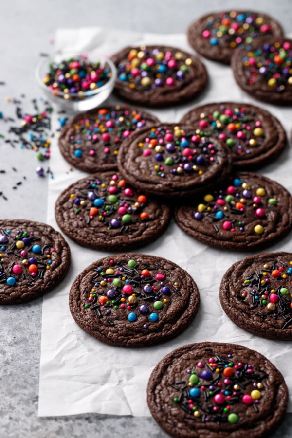 Assorted Sprinkle-topped Brownie Cookies scattered on a piece of crumpled parchment