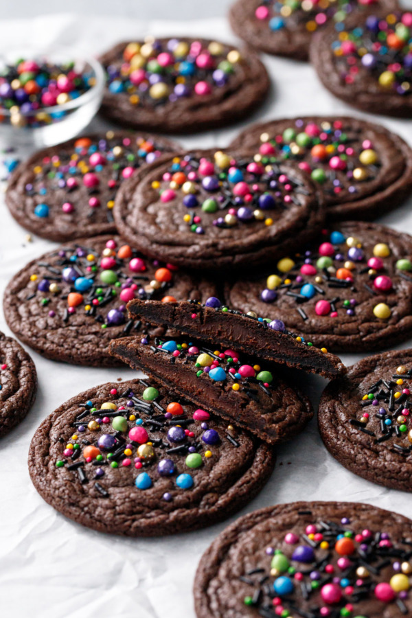 Scattered brownie cookies, one cookie cut in half to show the ganache filling.