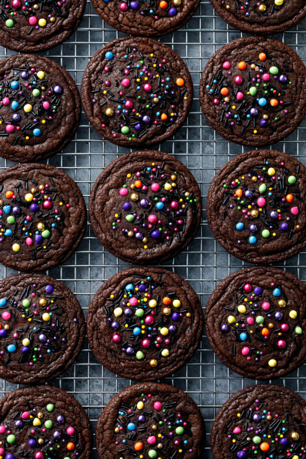 Overhead, cooling rack with an even grid of Ganache-Stuffed Cosmic Brownie Cookies topped with colorful sprinkles