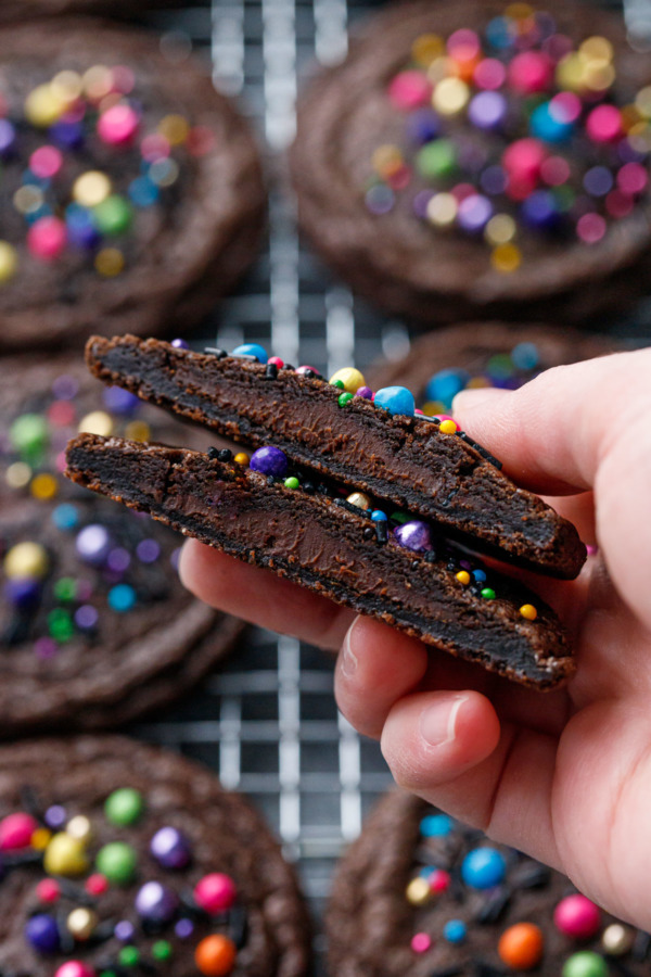 Hand holding a cut brownie cookie showing the chocolate ganache filling